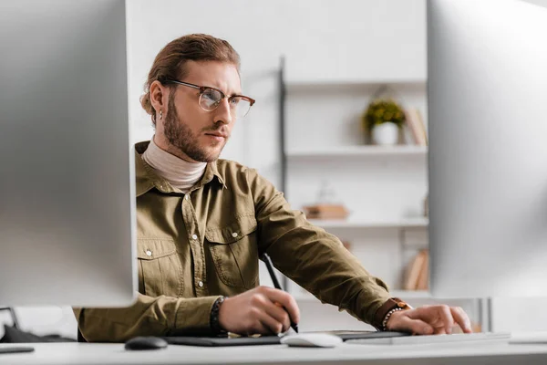 Selektiver Fokus des 3D-Künstlers, der auf den Computermonitor blickt, während er das Grafik-Tablet am Tisch benutzt — Stockfoto