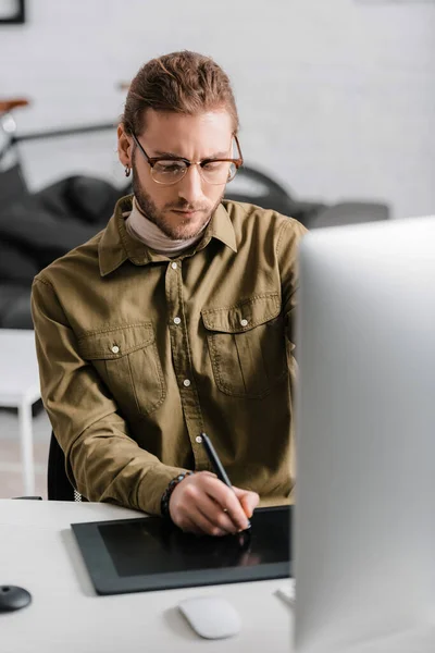 Selektiver Fokus eines gut aussehenden 3D-Künstlers mit einem Grafik-Tablet in der Nähe eines Computermonitors auf einem Tisch im Büro — Stockfoto