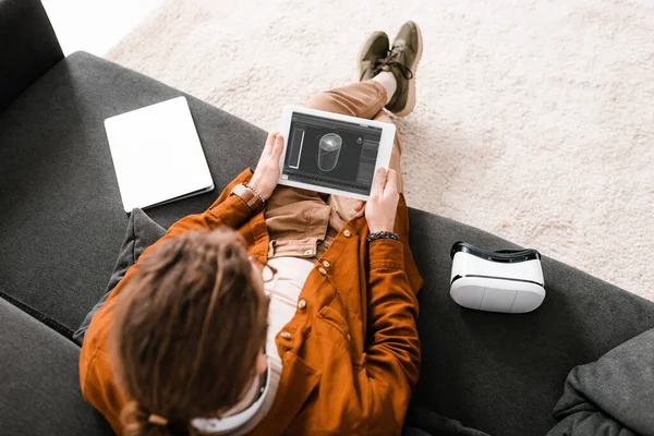 Вид зверху цифрового дизайнера, що тримає планшет з 3d дизайнерським проектом біля ноутбука та гарнітури vr на дивані — стокове фото