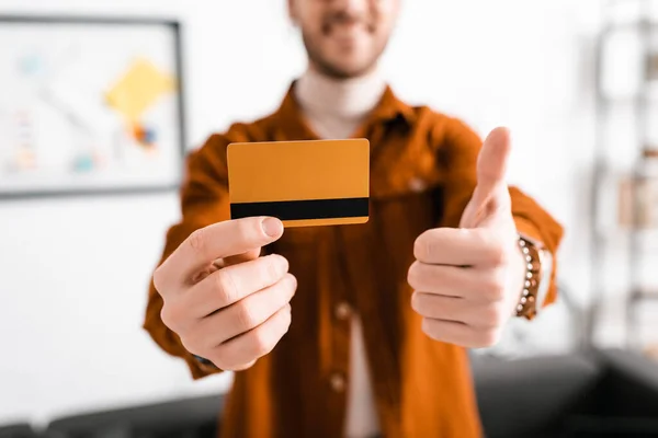 Selective focus of smiling 3d artist holding credit card and showing like gesture in office — Stock Photo