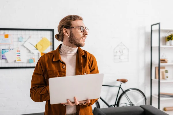 Bello artista 3d guardando lontano mentre si utilizza il computer portatile in ufficio — Foto stock