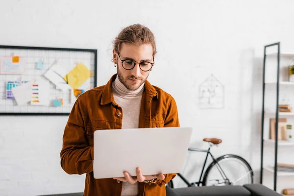 Diseñador digital guapo usando el ordenador portátil mientras trabaja en la oficina — Stock Photo