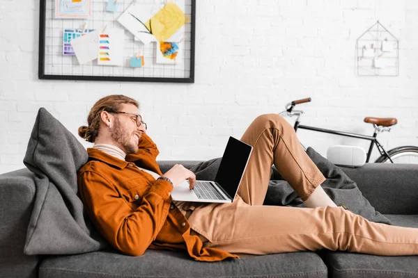 Side view of smiling 3d artist using laptop near vr headset on couch in office — Stock Photo