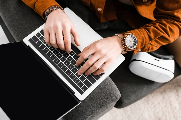 Vista de alto ângulo de artista 3d usando laptop com tela em branco perto de fone de ouvido realidade virtual no sofá — Fotografia de Stock