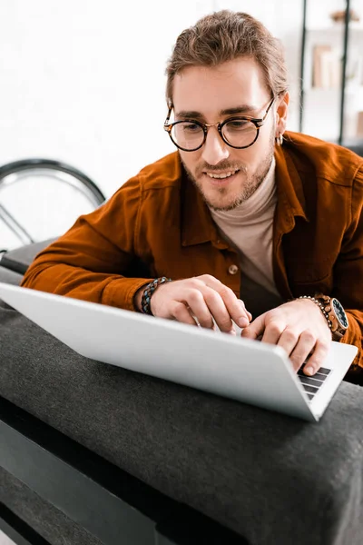 Selective focus of smiling 3d artist using laptop on couch in office — Stock Photo