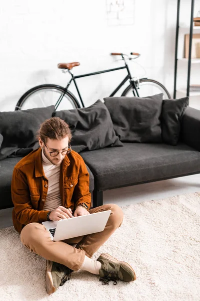 Handsome digital designer using laptop on floor near couch in office — Stock Photo