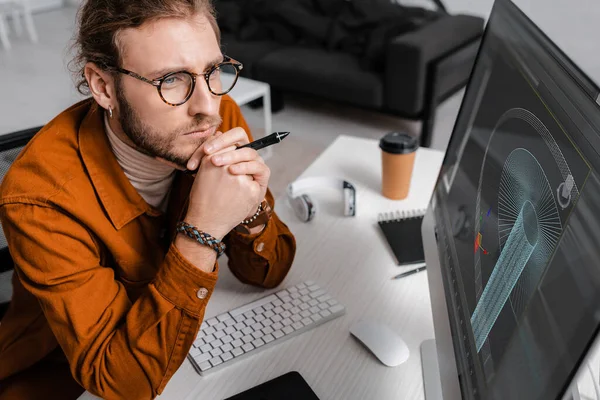 High angle view of thoughtful digital designer holding stylus near project of 3d design on computer monitor on table — Stock Photo