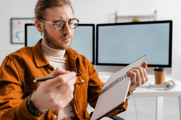 Selective focus of handsome digital designer holding pen and notebook in office — Stock Photo