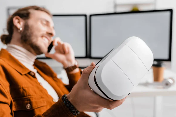 Selektiver Fokus eines lächelnden 3D-Künstlers, der auf dem Smartphone spricht und sein Headset im Büro hält — Stockfoto