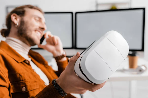 Selective focus of smiling 3d artist talking on smartphone and holding vr headset in office — Stock Photo