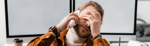 Панорамний знімок втомленого 3D-дизайнера, що розмовляє на смартфоні біля комп'ютерних моніторів в офісі — стокове фото