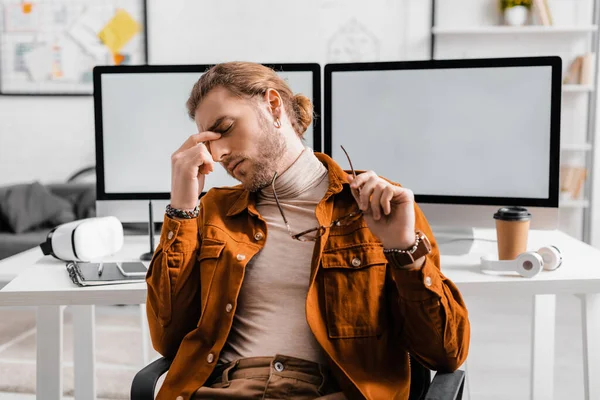 Tired 3d artist holding eyeglasses near digital devices on table in office — Stock Photo