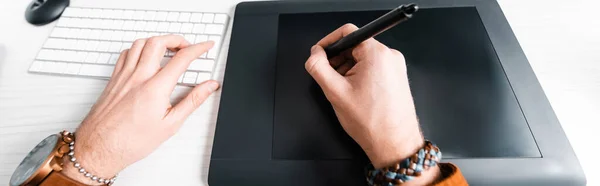 Обрезанный вид цифрового дизайнера, работающего с графическим планшетом и компьютерной клавиатурой за столом, панорамный снимок — стоковое фото