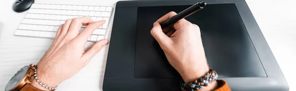 Vue recadrée du concepteur numérique travaillant avec tablette graphique et clavier d'ordinateur à la table, prise de vue panoramique — Photo de stock