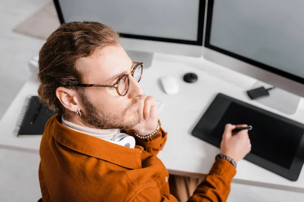 Enfoque selectivo del artista 3D pensativo mirando hacia otro lado mientras trabaja con tabletas gráficas y computadoras en la mesa - foto de stock