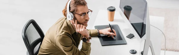 Панорамный снимок 3D художника в наушниках, работающего с графическими планшетами и компьютерами за столом — стоковое фото