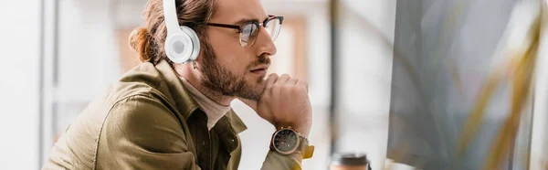 Side view of pensive 3d artist in headphones looking at computer monitor, panoramic shot — Stock Photo