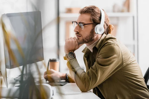 Side view of 3d artist in headphones using graphics tablet and looking at computer monitor on table — Stock Photo