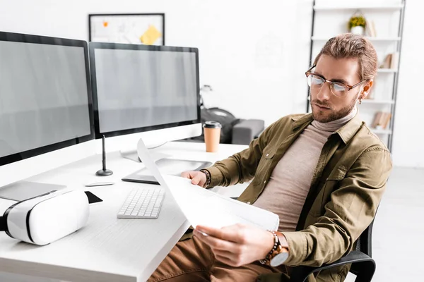 Diseñador digital que mira el plano mientras renderiza el proyecto de diseño 3d en computadoras en la mesa - foto de stock