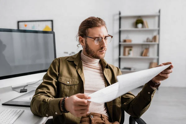 Selective focus of 3d artist looking at blueprint while working at table in office — Stock Photo