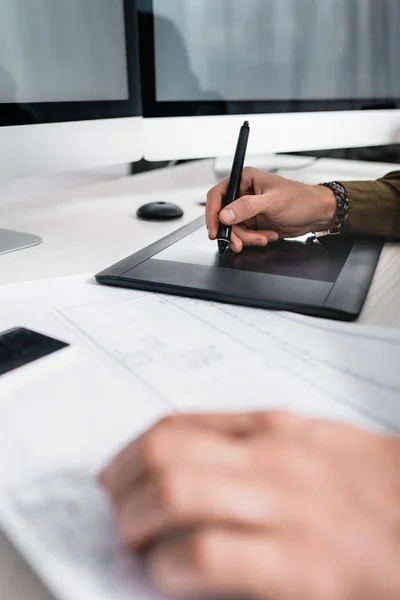 Selective focus of 3d artist using graphics tablet near blueprint while working at table — Stock Photo