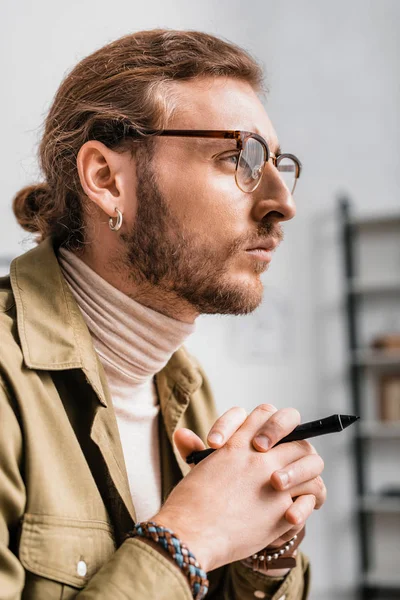 Side view of handsome 3d artist holding stylus of graphics tablet and looking away — Stock Photo