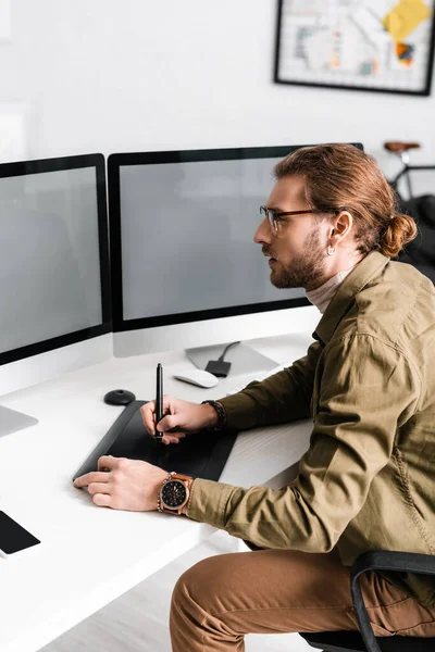 Side view of handsome digital designer working with graphics tablet and computers with blank screen on table — Stock Photo