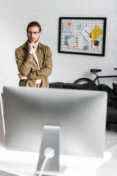 Selective focus of pensive 3d artist looking at computer monitor on table in office — Stock Photo