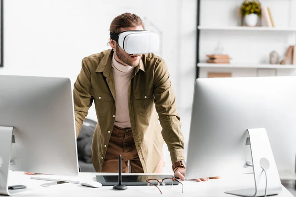 Progettista digitale in cuffia realtà virtuale in piedi vicino a computer e tablet grafico sul tavolo — Foto stock