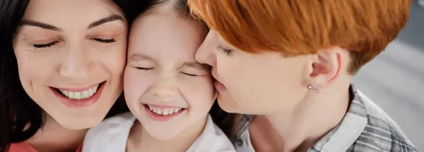 Panorâmica tiro de sorrir casal do mesmo sexo abraçando filha em casa — Fotografia de Stock