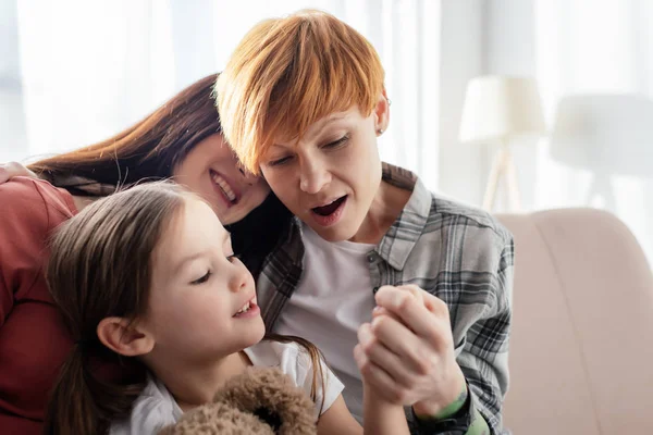 Shocked madre guardando mano di figlia con orsacchiotto vicino genitore sul divano — Foto stock