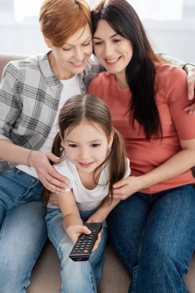 Focus selettivo del bambino sorridente con telecomando che guarda film vicino alle madri sul divano — Foto stock
