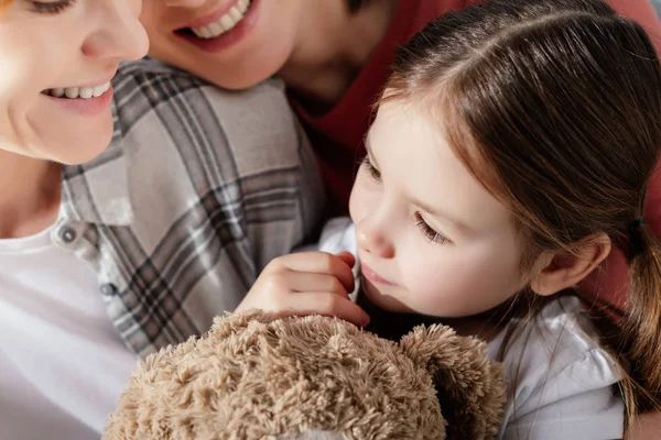 Criança com ursinho de pelúcia olhando para longe perto sorrindo pais do mesmo sexo — Fotografia de Stock