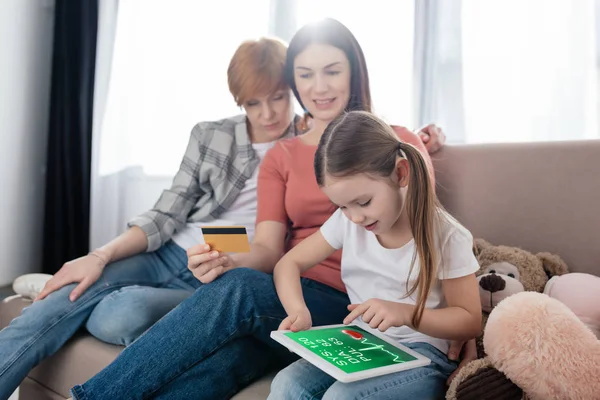 Enfant utilisant une tablette numérique avec application e-santé à l'écran près des mères avec carte de crédit à la maison — Photo de stock