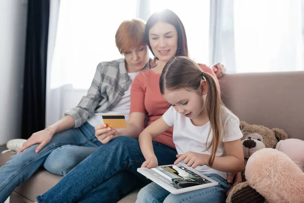 Kid using digital tablet with tickets app on screen near same sex parents with credit card at home — Stock Photo