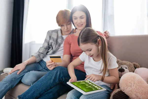 Child using digital tablet with e-health app on screen near same sex parents with credit card — Stock Photo