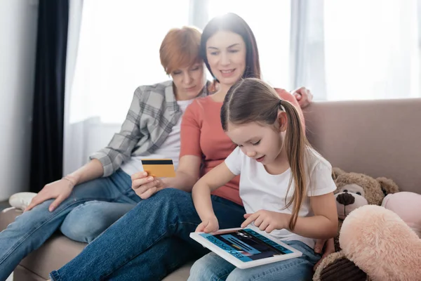 Kind nutzt digitales Tablet mit Buchungs-App am Bildschirm in der Nähe von Müttern mit Kreditkarte zu Hause — Stockfoto