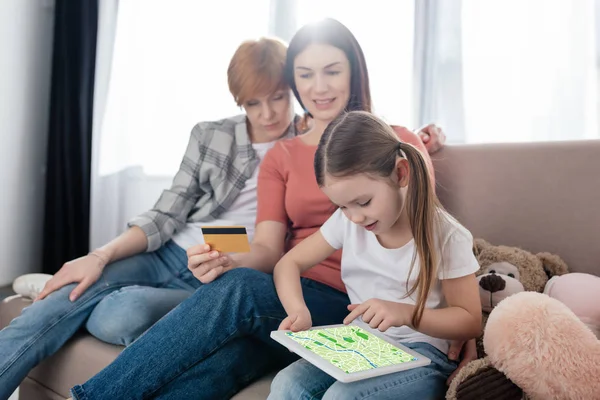 Child holding digital tablet with map app on screen near parents with credit card at home — Stock Photo