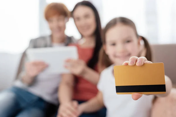 Selektiver Fokus des Kindes zeigt Kreditkarte in der Nähe von Müttern mit digitalem Tablet auf der Couch — Stockfoto