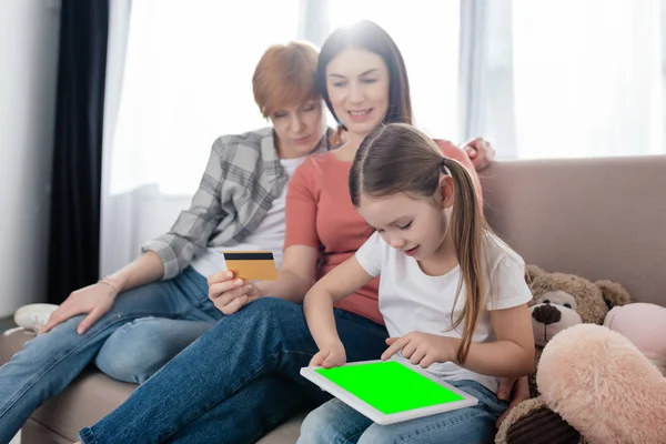 Kid using digital table with chroma key near mothers with credit card on couch — Stock Photo