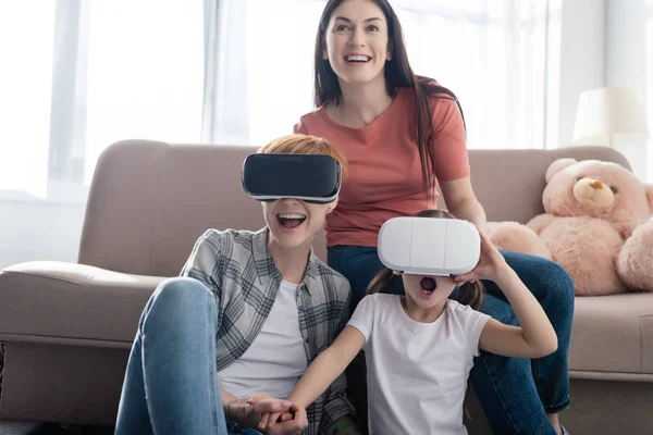 Shocked kid in vr headset holding hand of mother near parent at home — Stock Photo