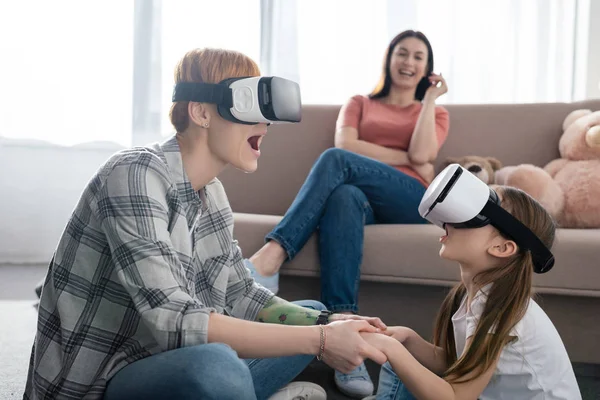 Selective focus of shocked mother and child using vr headsets near parent in living room — Stock Photo