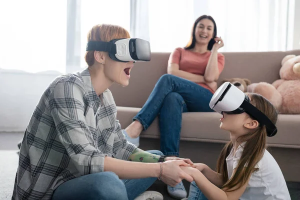 Concentration sélective de la mère et de l'enfant choqués en utilisant des casques vr près du parent dans le salon — Photo de stock