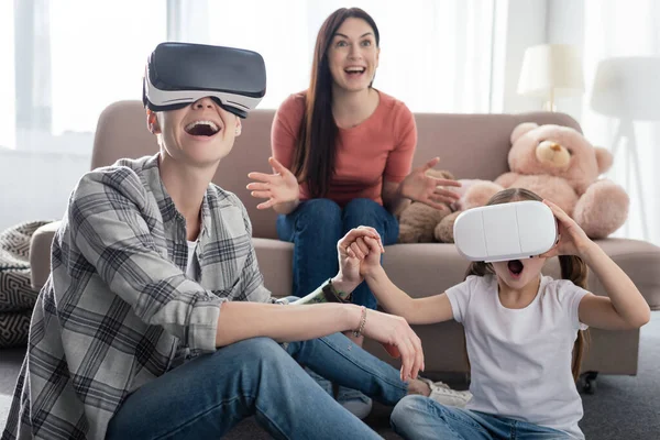 Same sex parents using virtual reality headsets with excited daughter in living room — Stock Photo