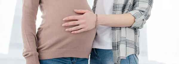 Cropped view of woman touching belly of pregnant girlfriend, panoramic shot — Stock Photo