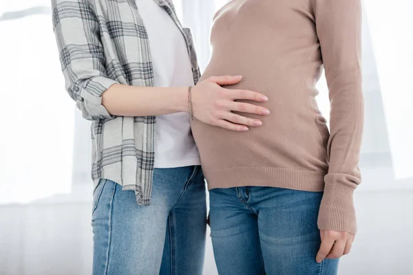 Ausgeschnittene Ansicht einer Frau, die den Bauch ihrer schwangeren Freundin zu Hause berührt — Stockfoto