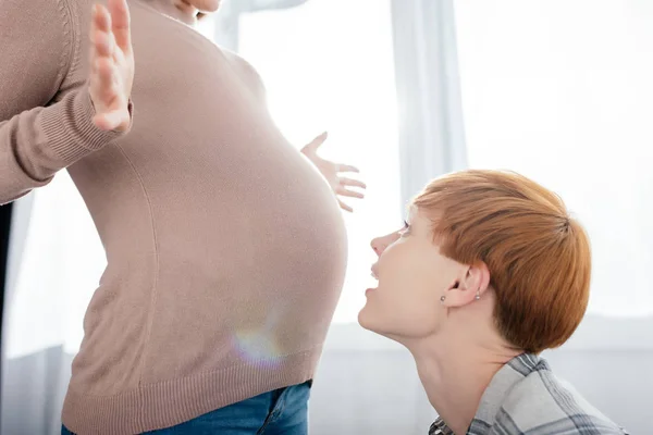 Vue latérale de la femme regardant le ventre de la petite amie enceinte à la maison — Photo de stock