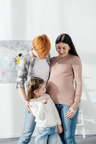 Enfant pointant du doigt sur le ventre de la mère enceinte près du parent dans le salon — Photo de stock