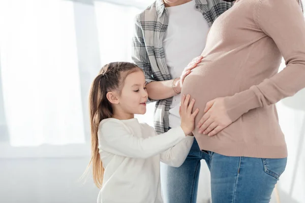 Ребенок и родитель трогают живот беременной матери в гостиной — стоковое фото