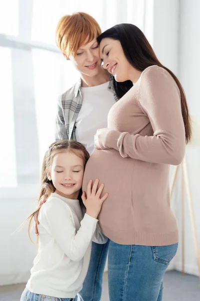Sonriente niño tocando el vientre de la madre embarazada cerca de los padres en casa - foto de stock